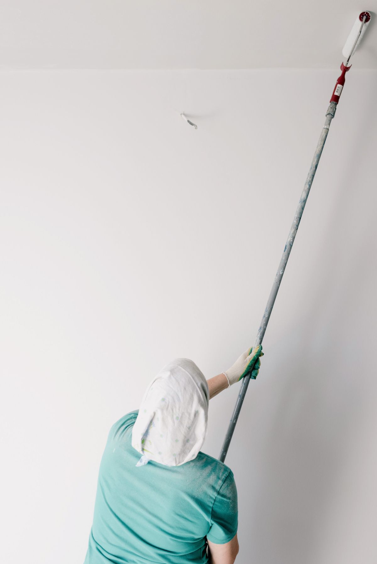 Painter using an extension-pole roller to apply white paint to a ceiling