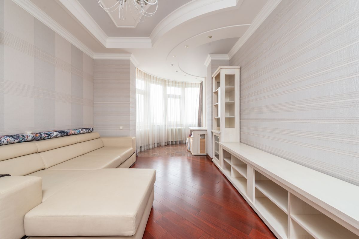 Sitting room with a smooth white multi-level ceiling, cove details, and warm wood floor